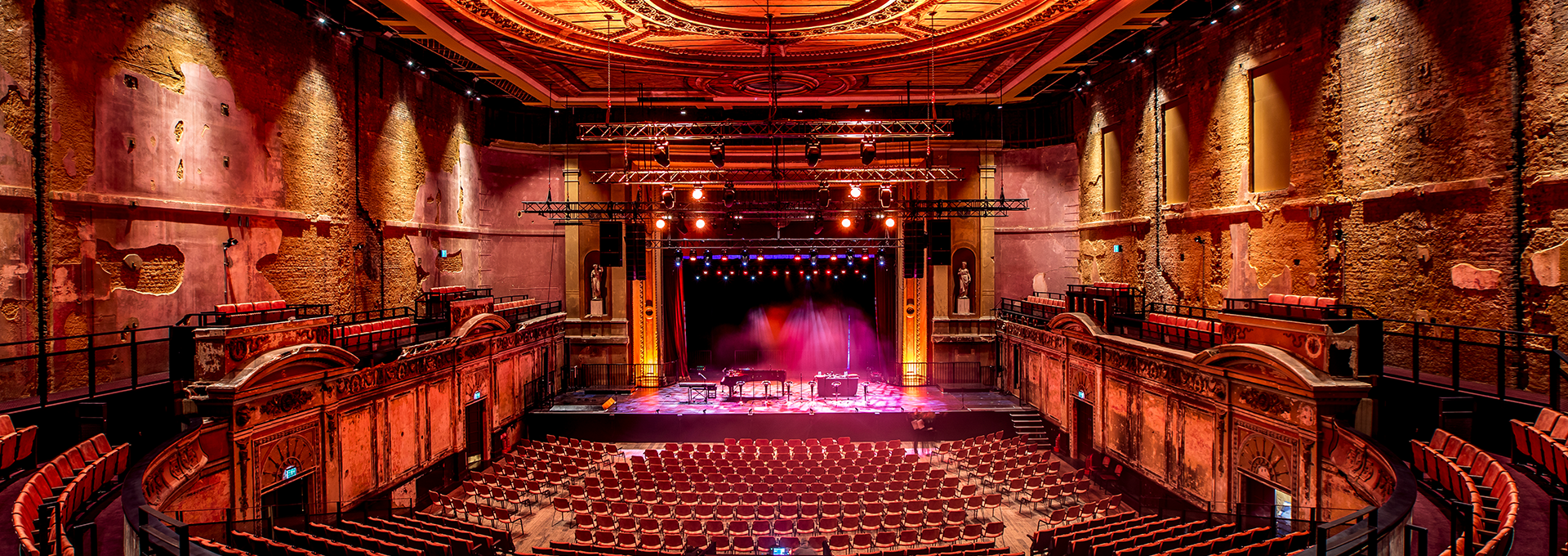 Empty auditorium lit with red lighting viewing the stage with pink lighting.