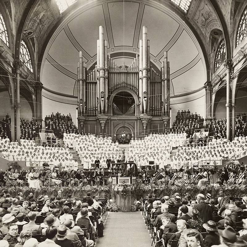 Audience in large concert space watching a performance of a large organ.