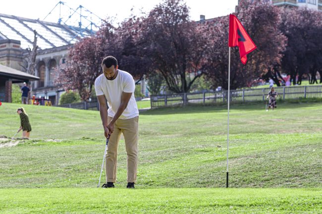 Man putting a golf ball into a hole on a golf course.
