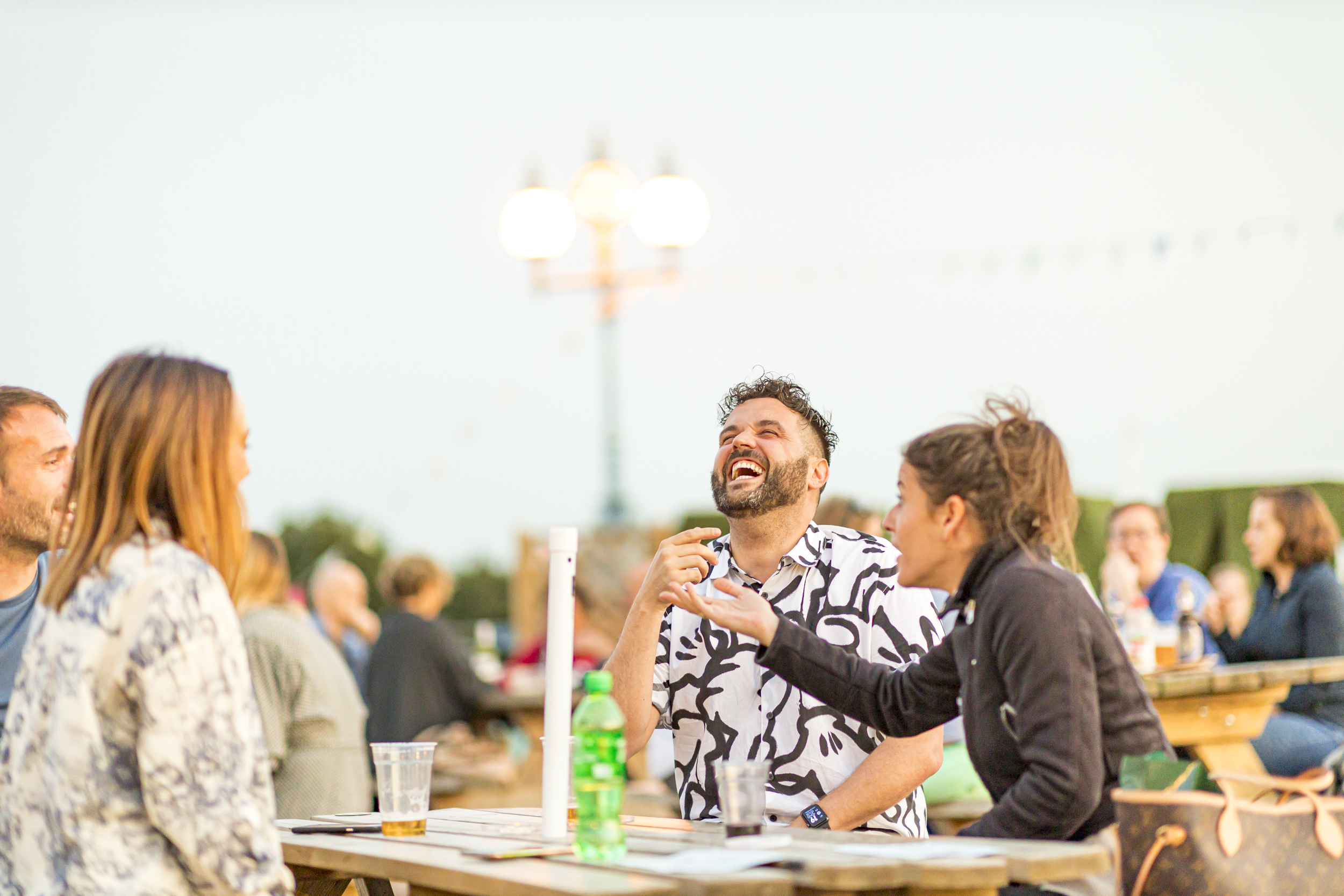 People sitting at a picnic table on a sunny evening laughing and enjoying drinks