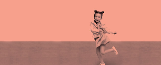 Ally Pally Performing Arts School. A smiling child with pigtails and a denim jacket twirls joyfully on a peach-colored background, conveying a sense of happiness and playfulness.