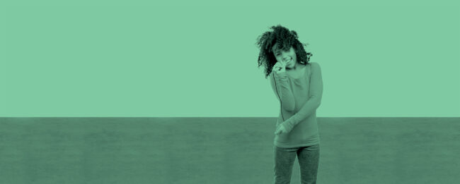 A child in a long-sleeved shirt joyfully sings into a pen as a microphone, against a green background, conveying a playful, carefree mood.